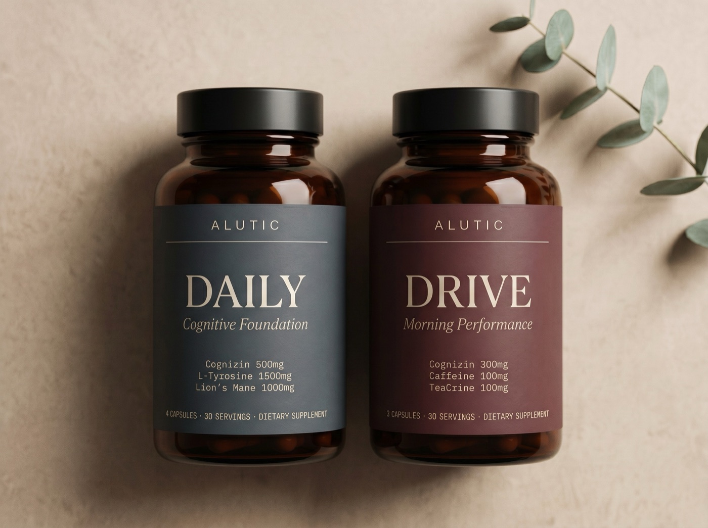 The Alutic Bundle: the Daily slate-label bottle and the Drive oxblood-label bottle side by side on a warm neutral surface beside a eucalyptus sprig.