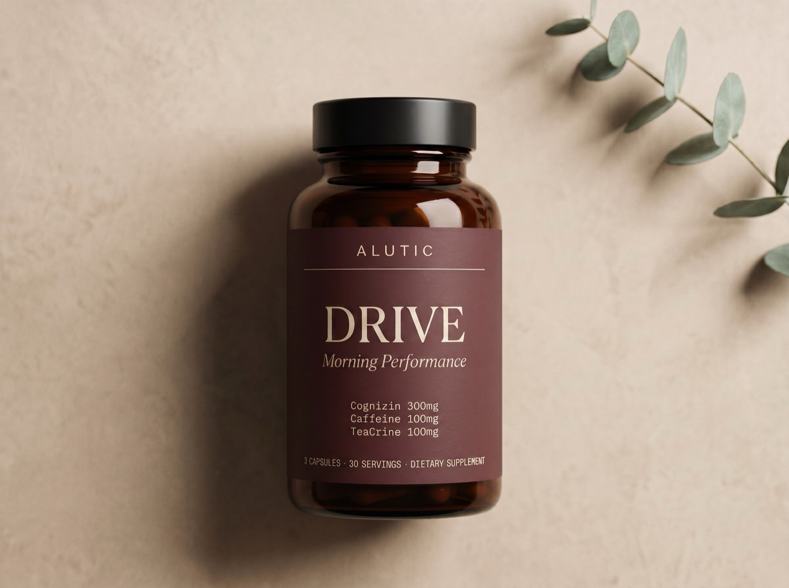 Alutic Drive, an amber glass supplement bottle with a deep oxblood label, on a warm neutral surface beside a eucalyptus sprig.
