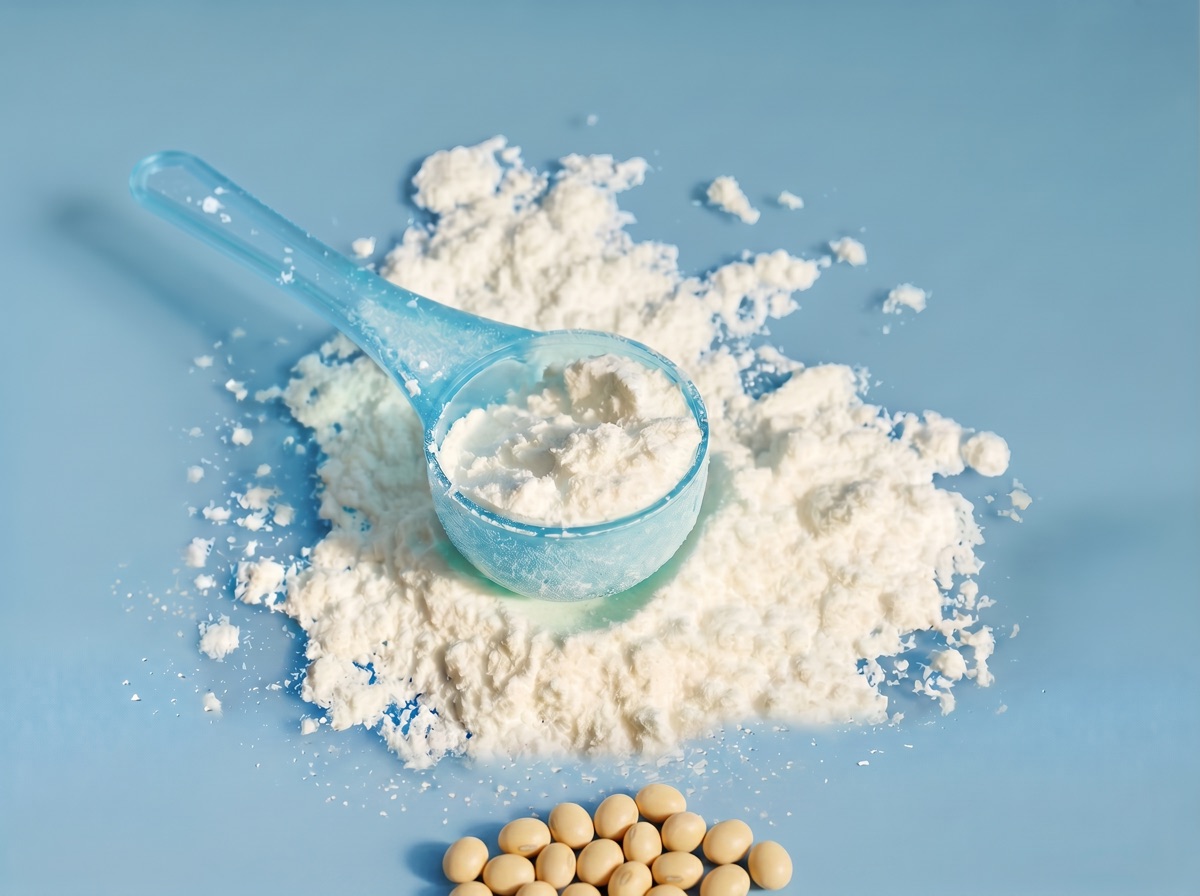 A translucent blue scoop of pale white phosphatidic acid powder with whole dried soybeans at the bottom edge on a muted blue studio background.