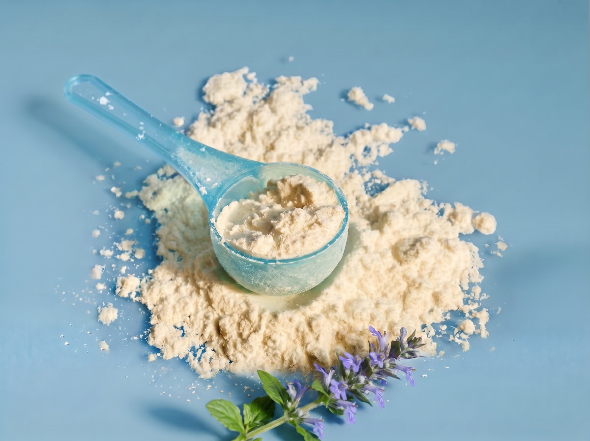 A translucent blue scoop of pale Turkesterone extract powder with a purple-flowered Ajuga turkestanica sprig at the bottom edge on a muted blue studio background.