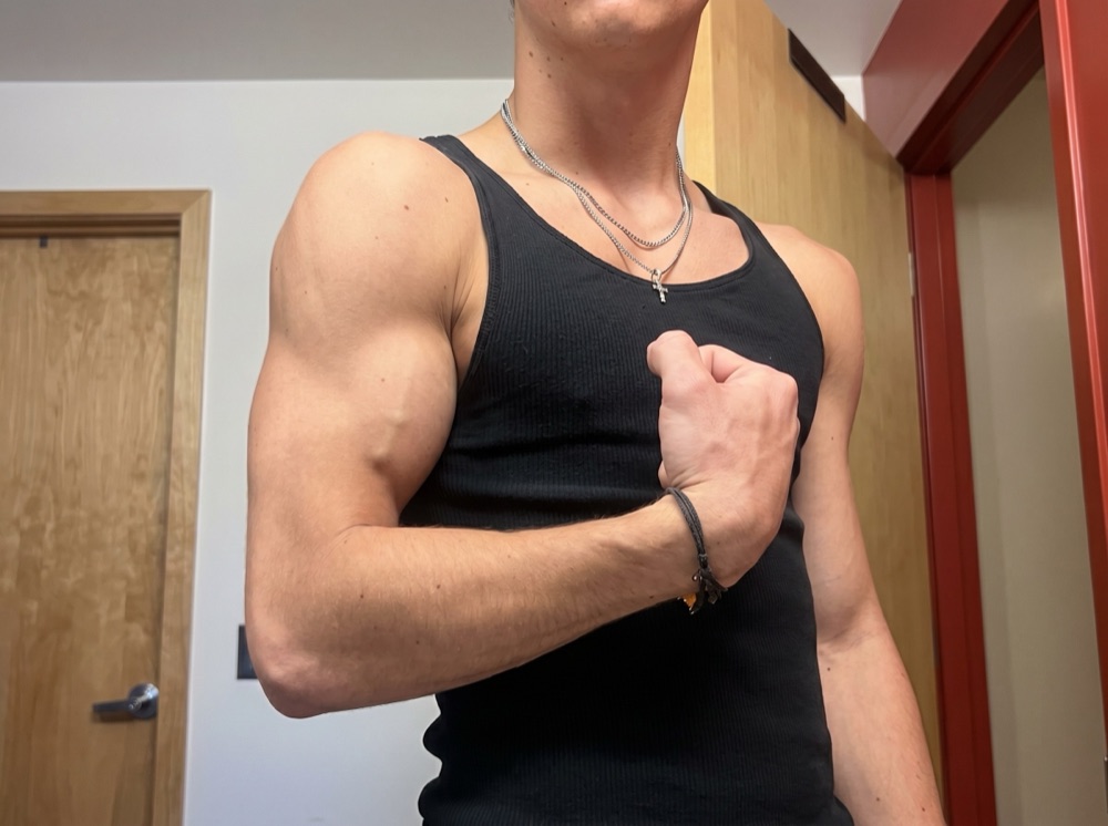 Before photo: young man in a tank top, flexing his arm to show baseline muscle development.